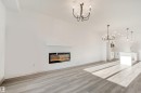 Spacious room with wood-finish flooring, a wall-mounted linear fireplace, and modern chandeliers - 1515 211 Street Nw, Edmonton, AB 