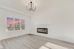 Spacious room featuring wood-finish flooring, a contemporary chandelier, a built-in electric fireplace with a floating mantel, and multiple windows - 