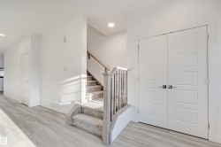 Wood-finish flooring with a carpeted staircase featuring a wood handrail and iron balusters - 