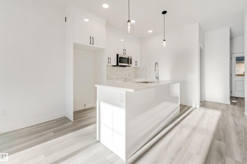 Modern kitchen featuring white cabinetry, a large island with an undermount sink, stainless steel microwave, and wood-finish flooring - 1515 211 Street Nw, Edmonton, AB 