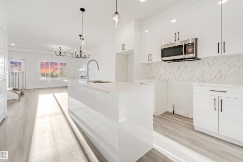 Modern kitchen featuring white cabinetry, a large kitchen island with an integrated sink, and stainless steel microwave - 1515 211 Street Nw, Edmonton, AB 