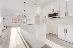 Modern kitchen featuring white cabinetry, a large kitchen island with an integrated sink, and stainless steel microwave - 