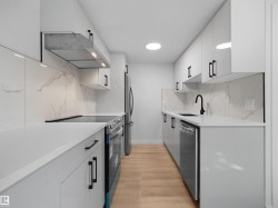 Sleek kitchen featuring white cabinetry, light-toned countertops, a stainless steel range hood, and a black matte faucet, complemented by wood-finish flooring - 