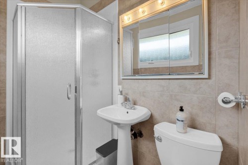 Frosted glass shower enclosure, pedestal sink, wall-mounted mirrored medicine cabinet, integrated vanity lighting, and ceramic tile wainscoting - 15012 77 Avenue Nw, Edmonton, AB 