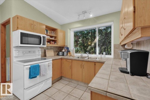 Kitchen featuring extensive wood cabinetry, tile countertops, built-in dual basin sink, tile flooring, and a large window - 15012 77 Avenue Nw, Edmonton, AB 