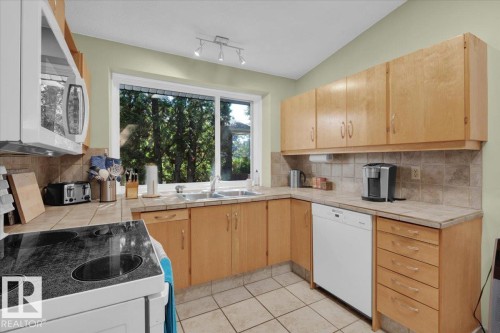 Kitchen featuring wood-finish cabinetry, tile flooring, tile countertops, a tile backsplash, and a window above the sink - 15012 77 Avenue Nw, Edmonton, AB 