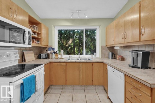 U-shaped kitchen layout with wood-finish cabinetry, tile flooring, and a tile backsplash - 15012 77 Avenue Nw, Edmonton, AB 
