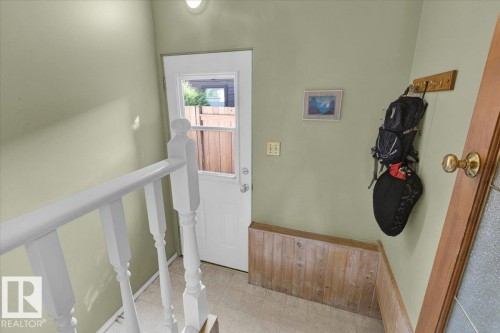White painted banister, white paneled door with window, light-colored flooring, light green walls, and wood paneling - 15012 77 Avenue Nw, Edmonton, AB 