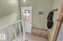 White painted banister, white paneled door with window, light-colored flooring, light green walls, and wood paneling - 