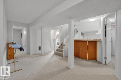 Finished basement space featuring light-toned carpeting and a built-in wood-finish bar - 15012 77 Avenue Nw, Edmonton, AB 