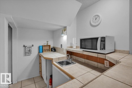 Compact kitchen area featuring tile countertops, a stainless steel sink, and wood-finish cabinetry - 15012 77 Avenue Nw, Edmonton, AB 