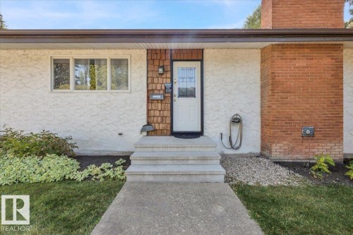 Exterior featuring a white entry door with decorative glass, cedar shake siding accents, and a brick chimney - 15012 77 Avenue Nw, Edmonton, AB 