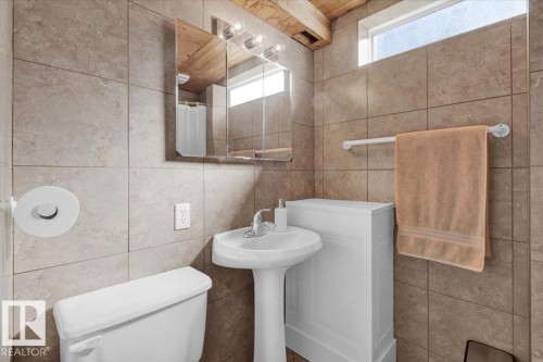 Pedestal sink with chrome faucet, medicine cabinet with integrated lighting, tiled walls, and a transom window providing natural light - 15012 77 Avenue Nw, Edmonton, AB 