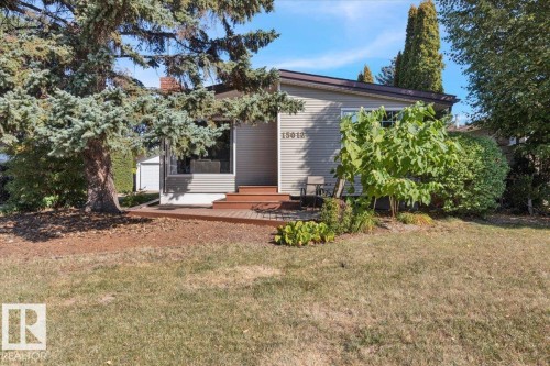 Siding exterior with a prominent picture window, wood-finish deck with steps, and mature evergreen and deciduous trees - 15012 77 Avenue Nw, Edmonton, AB 