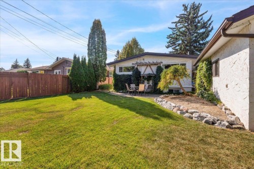 Expansive manicured lawn with a wooden privacy fence, mature trees, and a rock-lined garden bed - 15012 77 Avenue Nw, Edmonton, AB 