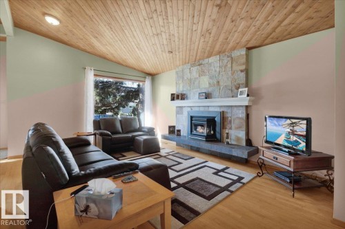 Angled wood-plank ceiling, wood-finish flooring, stone-clad fireplace with mantel, and large picture window - 15012 77 Avenue Nw, Edmonton, AB 