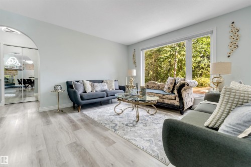 Light wood-finish flooring throughout, paired with a large picture window, an arched doorway, and white baseboards - #37 23020 Township Road 522 Rd, Rural Strathcona County, AB 