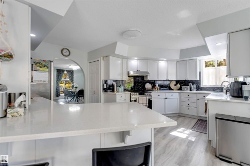 Kitchen featuring white cabinetry, light-toned countertops, a dark backsplash, stainless steel appliances, and wood-finish flooring - #37 23020 Township Road 522 Rd, Rural Strathcona County, AB 