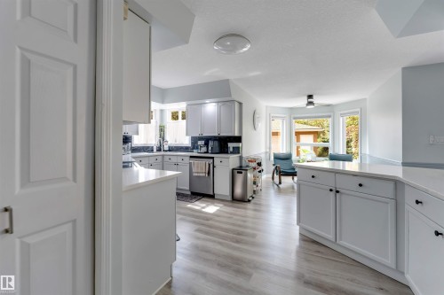 White cabinetry with dark hardware, stainless steel appliances, light-toned wood-finish flooring, and a bay window - #37 23020 Township Road 522 Rd, Rural Strathcona County, AB 