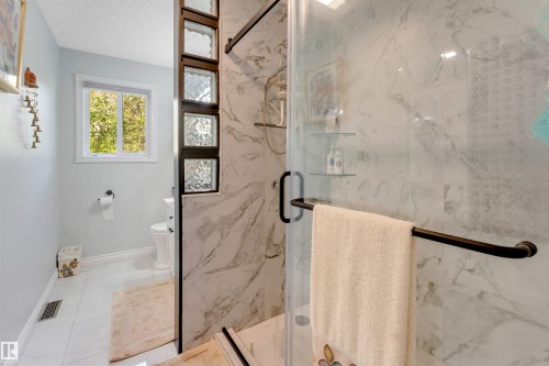 Glass-enclosed shower with marble-finish wall tiling, featuring a built-in shelf - #37 23020 Township Road 522 Rd, Rural Strathcona County, AB 