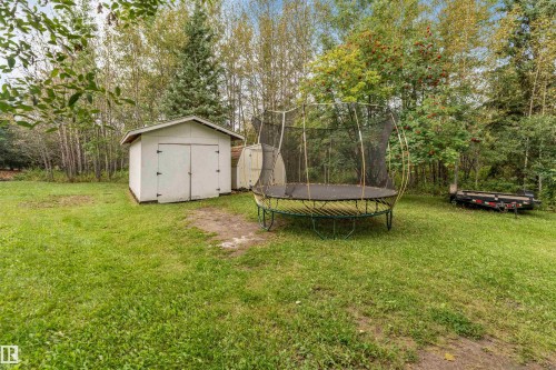 Expansive grassy area featuring a white storage shed with double doors and a sloped roof, complemented by mature trees - #37 23020 Township Road 522 Rd, Rural Strathcona County, AB 