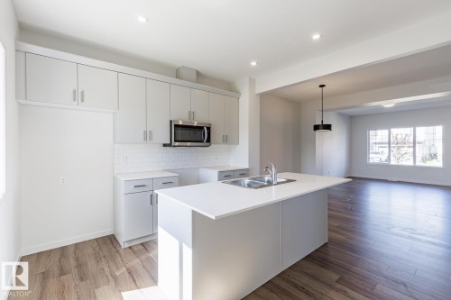 Kitchen with light-toned cabinetry, stainless steel microwave, and white tile backsplash - 3611 Triomphe Boulevard, Beaumont, AB 