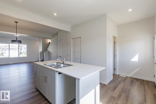 Kitchen island with a double basin sink, light-toned countertops, and recessed lighting - 3611 Triomphe Boulevard, Beaumont, AB 