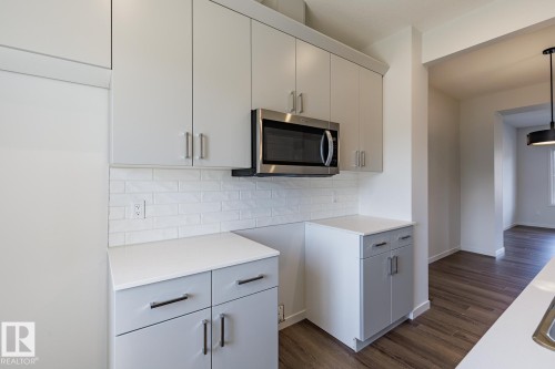 Light gray cabinetry with brushed nickel hardware, white countertop surfaces, white subway tile backsplash, stainless steel microwave, and wood-finish flooring - 3611 Triomphe Boulevard, Beaumont, AB 