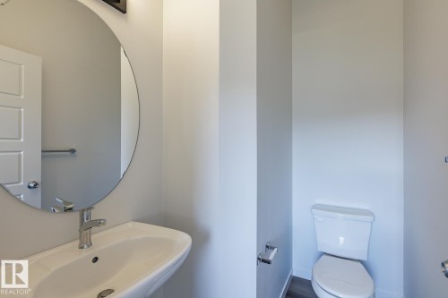 Wall-mounted sink with chrome faucet, circular mirror, and wood-finish flooring - 3611 Triomphe Boulevard, Beaumont, AB 