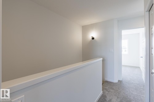 Wall-mounted sconce lighting, light gray wall paint, and gray textured carpeting - 3611 Triomphe Boulevard, Beaumont, AB 