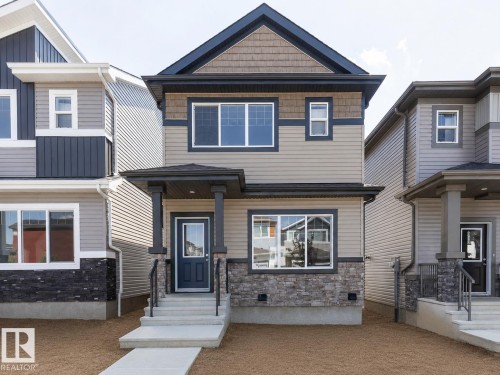 Two-story residence featuring a covered front porch, stone and siding exterior, front entry door with transom window, and a concrete walkway - 3611 Triomphe Boulevard, Beaumont, AB 