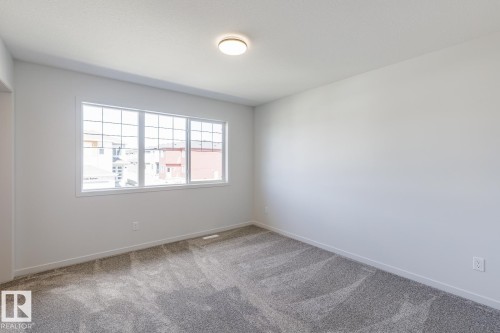 Neutral wall paint, gray patterned carpet, ceiling-mounted light fixture, and a large multi-pane window - 3611 Triomphe Boulevard, Beaumont, AB 