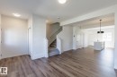 Wood-finish flooring throughout, bright white walls, staircase with carpeted treads, kitchen island with sink, and a modern pendant light fixture - 3611 Triomphe Boulevard, Beaumont, AB 