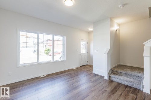 Expansive window with grid panes, wood-finish flooring, white trim, carpeted stairs, and a white entrance door with decorative glass - 3611 Triomphe Boulevard, Beaumont, AB 