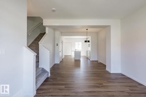 Wood-finish flooring, staircase with carpeted treads and painted railings, white interior walls, recessed lighting, and a black drum pendant light - 3611 Triomphe Boulevard, Beaumont, AB 