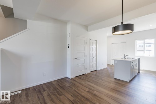 Wood-finish flooring throughout, white interior doors, and a modern island with an integrated sink and base cabinetry - 3611 Triomphe Boulevard, Beaumont, AB 