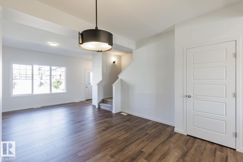Spacious interior featuring wood-finish flooring, white trim, recessed lighting, and a contemporary drum pendant light - 3611 Triomphe Boulevard, Beaumont, AB 