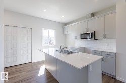 Kitchen featuring an island with a dual-basin stainless steel sink, light grey cabinetry, white subway tile backsplash, and wood-finish flooring - 