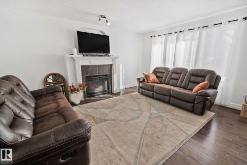 Living room with a fireplace featuring a white mantel and tile surround, recessed lighting, and dark wood-finish flooring - 1115 61 Street Sw, Edmonton, AB 