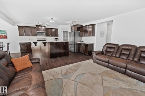 Open-concept living area with wood-finish flooring, dark wood cabinetry, stainless steel appliances, and a white subway tile backsplash - 1115 61 Street Sw, Edmonton, AB 