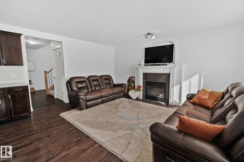 Dark wood-finish flooring, white walls, built-in fireplace with tile surround, white mantel, dark wood cabinetry with light countertop, and light-colored subway tile backsplash - 1115 61 Street Sw, Edmonton, AB 