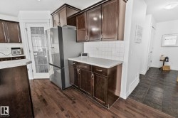 Rich wood-finish flooring, dark wood cabinetry, white tile backsplash, and light-toned countertops - 
