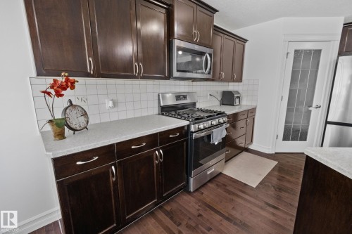 Dark wood-finish cabinetry with modern hardware, white tile backsplash, light-toned countertops, and stainless steel appliances - 1115 61 Street Sw, Edmonton, AB 