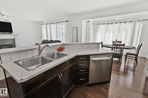 Kitchen island with dual stainless steel sink, integrated dishwasher, and dark wood cabinetry - 1115 61 Street Sw, Edmonton, AB 