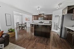 Hardwood flooring throughout the main living areas, a kitchen island with seating, dark wood-finish cabinetry, a white subway tile backsplash, and stainless-steel appliances - 