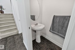Pedestal sink with chrome faucet, oval wall mirror, and dark tile flooring - 