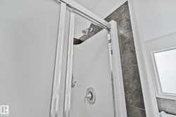 Shower enclosure with sliding glass door, chrome shower head, and gray tiled wall - 