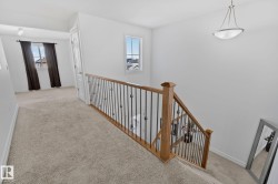 Carpeted hallway featuring a wood and wrought iron staircase railing, a window, and a ceiling-mounted light fixture - 