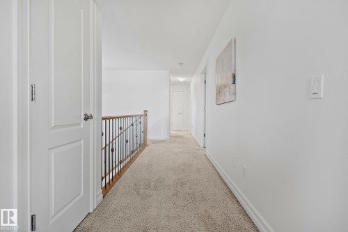 Neutral-toned wall-to-wall carpeting, white interior doors with contemporary hardware, and a wood and wrought iron staircase railing - 1115 61 Street Sw, Edmonton, AB 