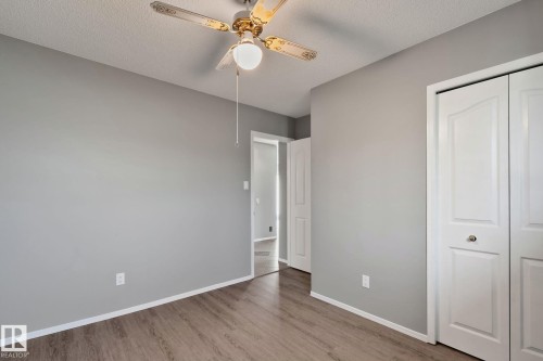 Wood-finish flooring, light grey painted walls, white bi-fold closet doors, and an overhead ceiling fan with light fixture - 14724 73 Street Nw, Edmonton, AB 
